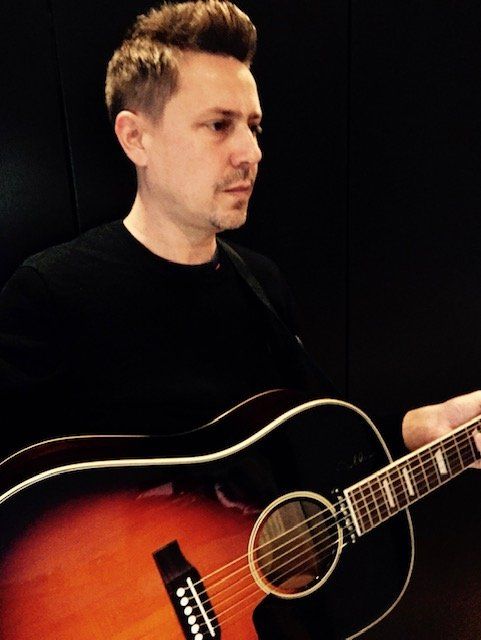 A man in a black shirt is holding an acoustic guitar