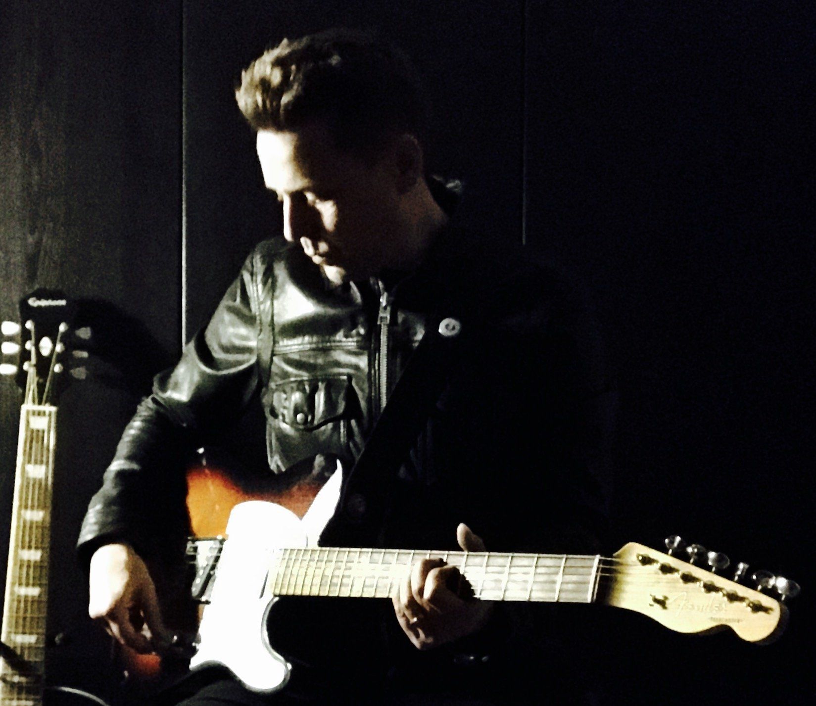 A man in a leather jacket is playing an electric guitar