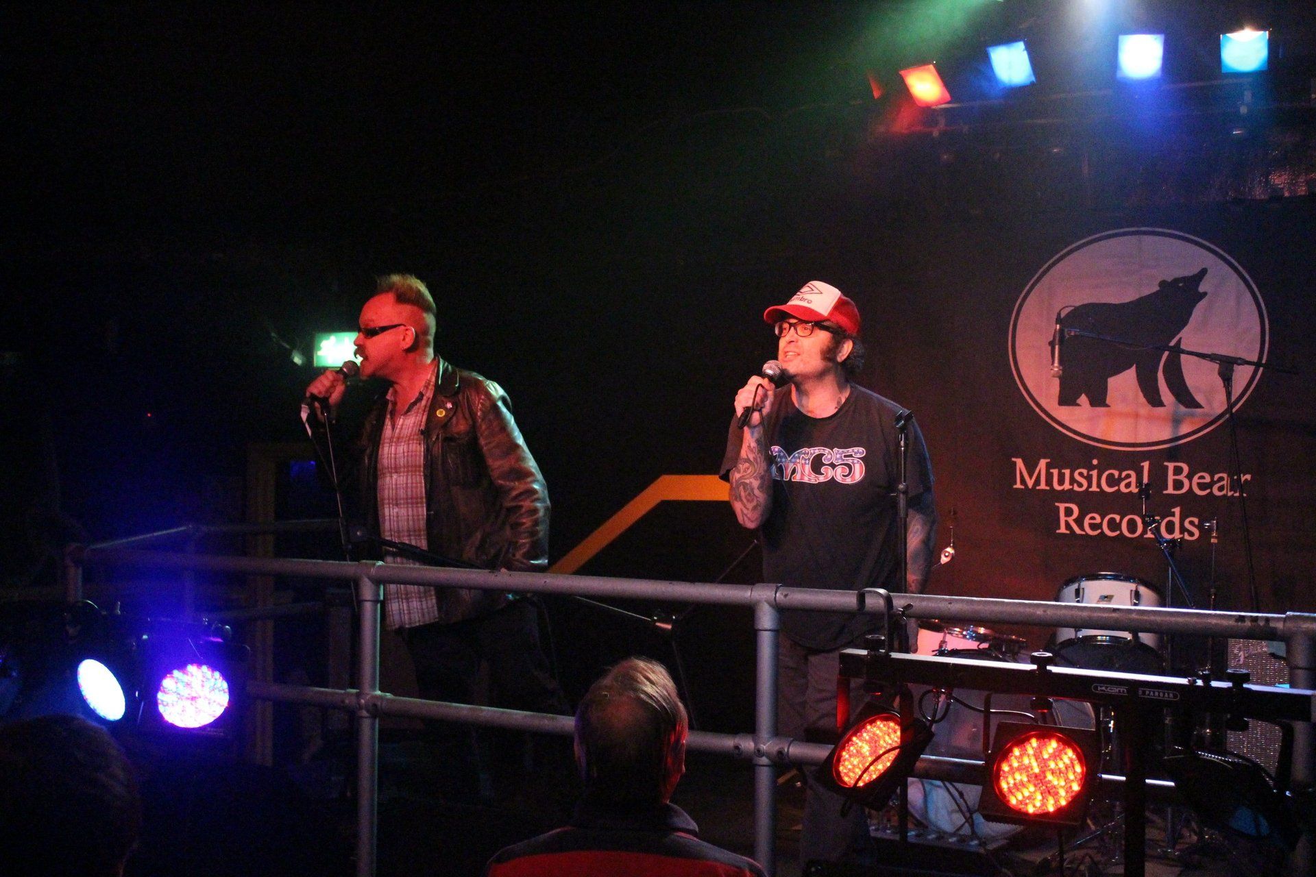 Two men singing on stage in front of a sign that says musical bear records
