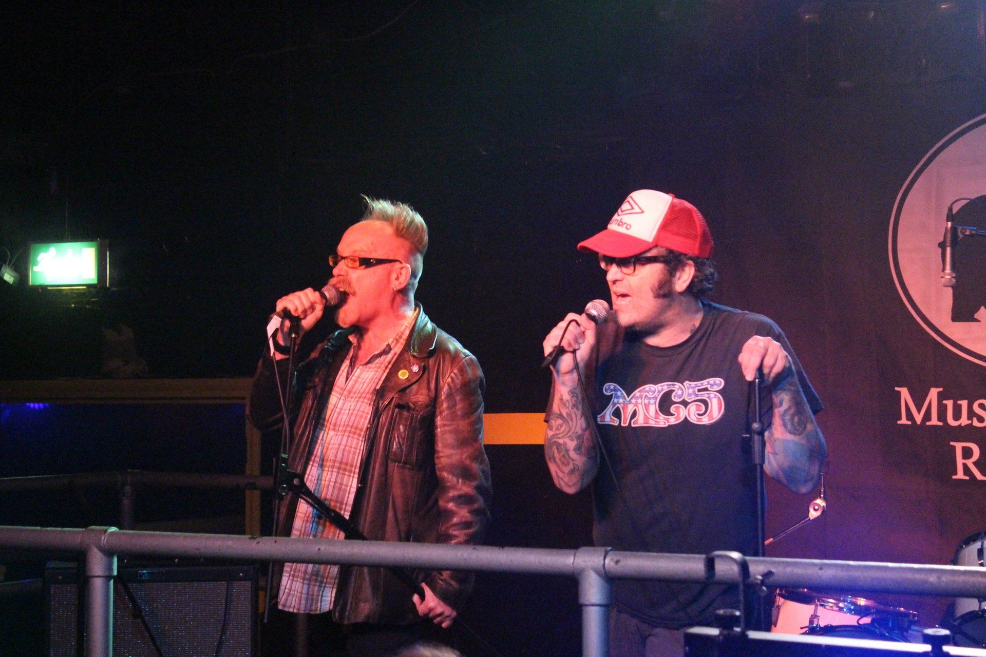 Two men singing into microphones in front of a sign that says muse
