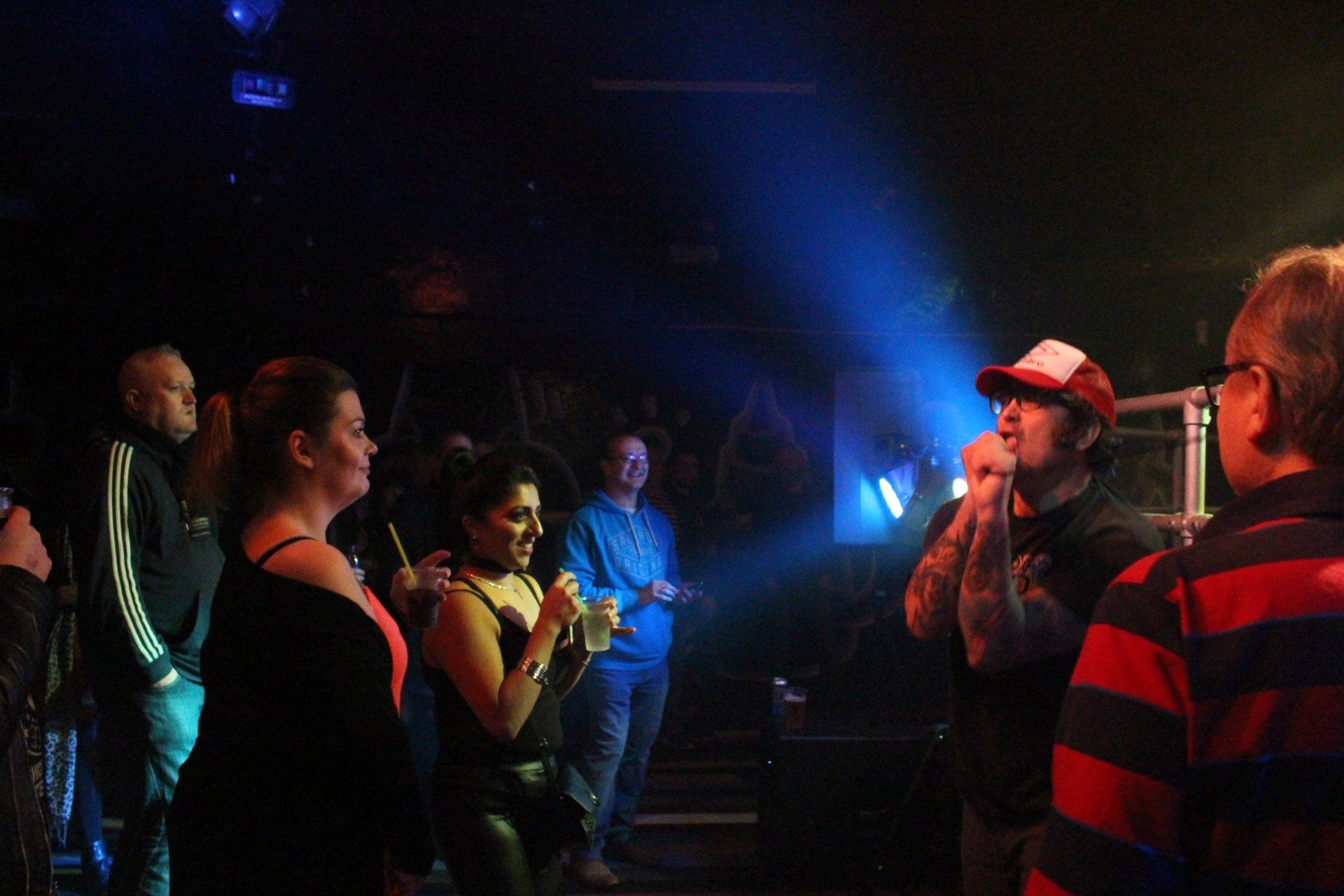 A group of people are standing in a dark room watching a man sing into a microphone.