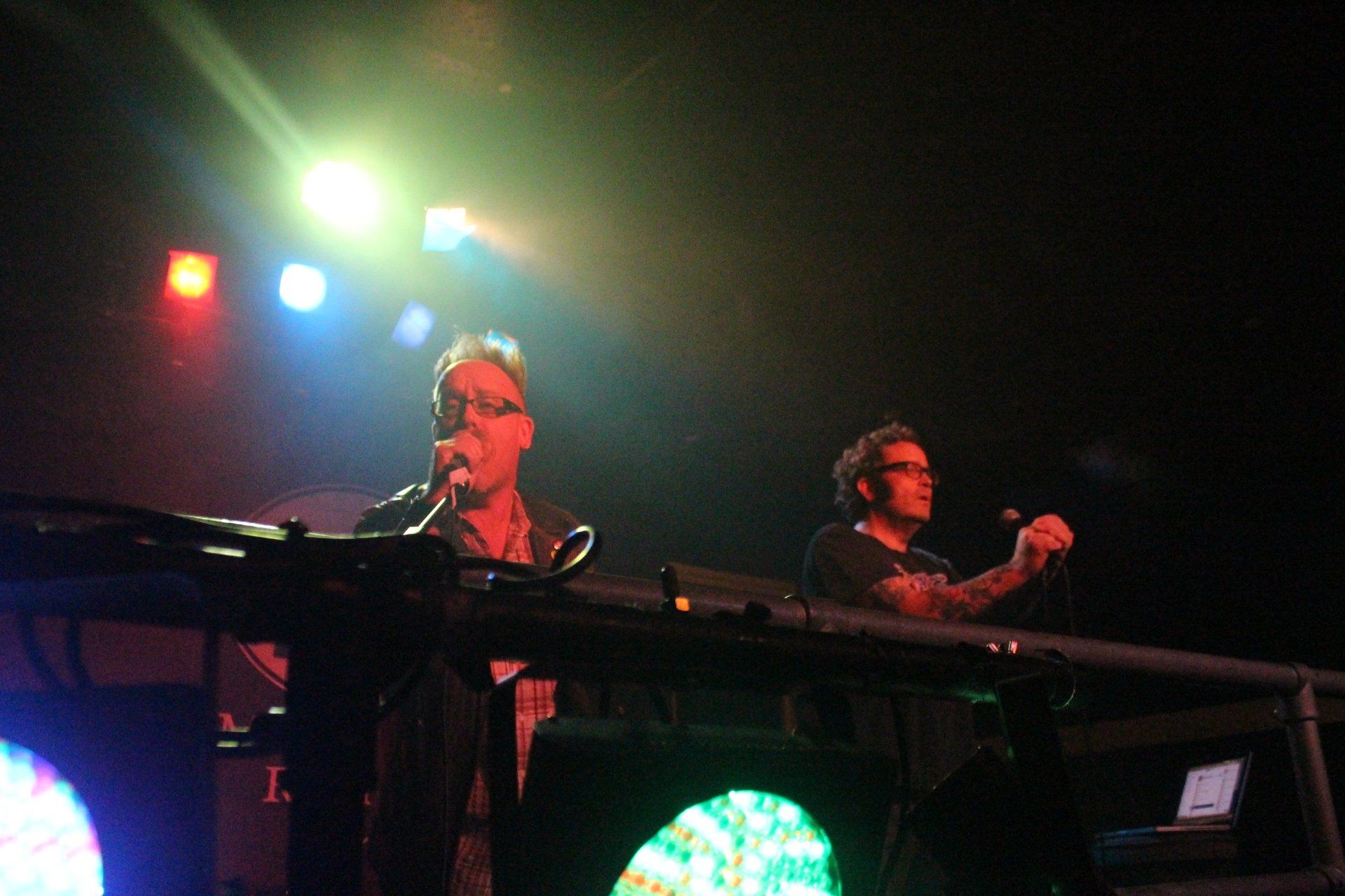 Two men are playing keyboards on a stage in a dark room.