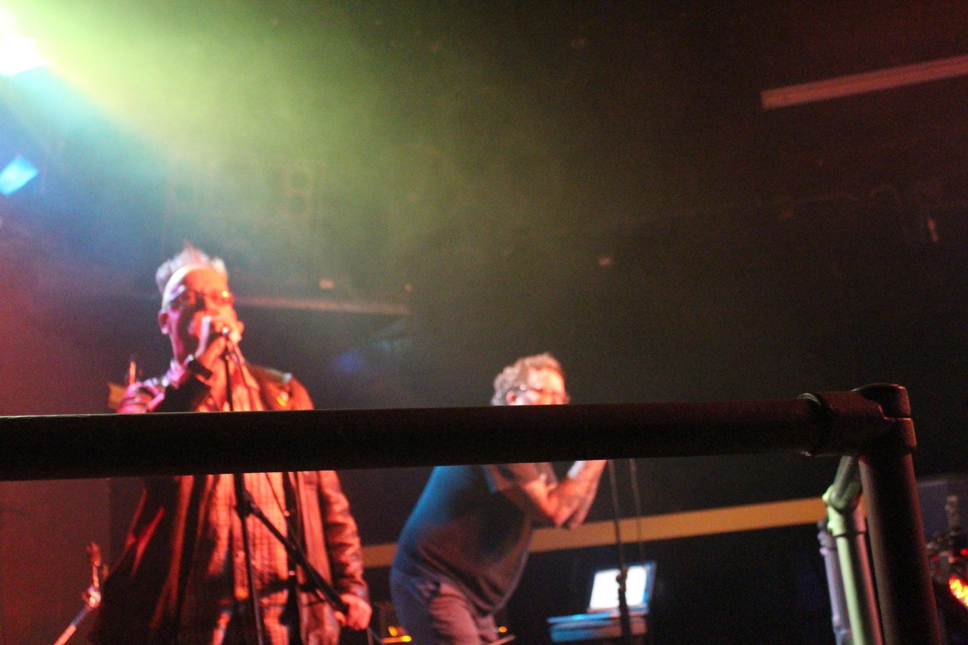 Two men singing into microphones on a stage in a dark room