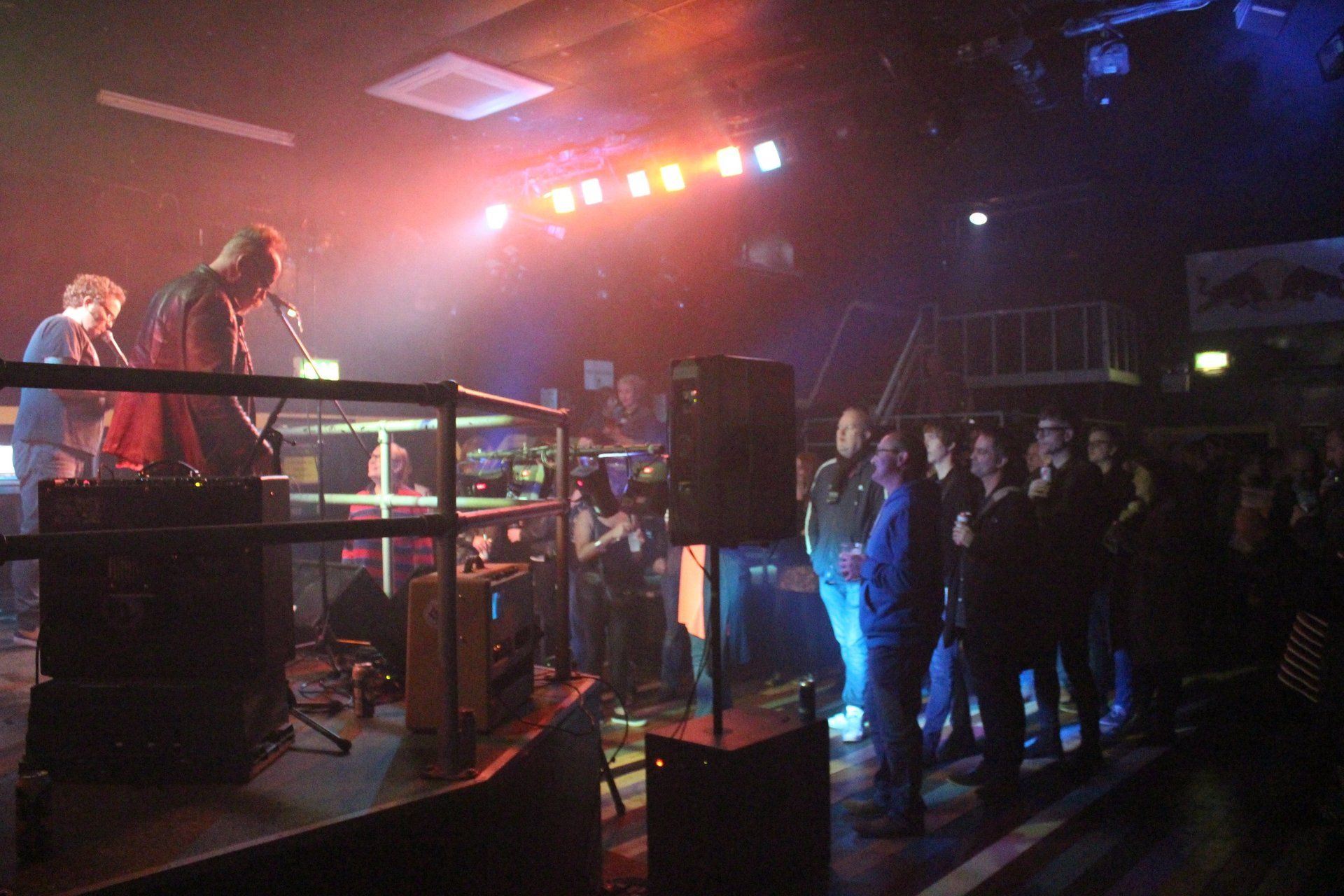 A group of people are standing in front of a stage in a dark room.