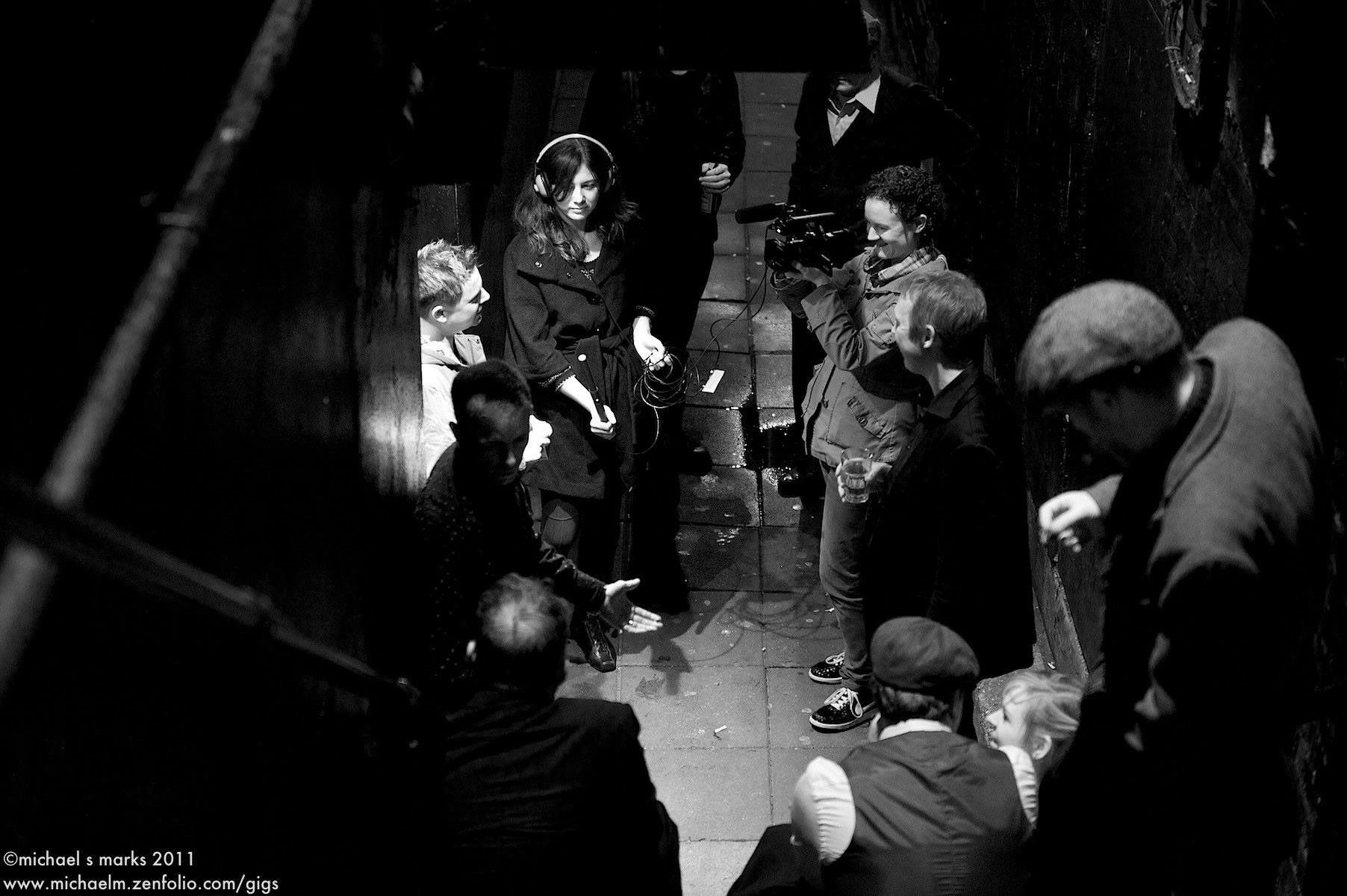 A black and white photo of a group of people standing on a sidewalk.