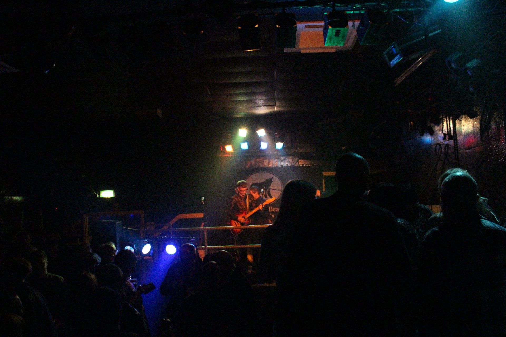 A man is playing a guitar in front of a crowd of people in a dark room.