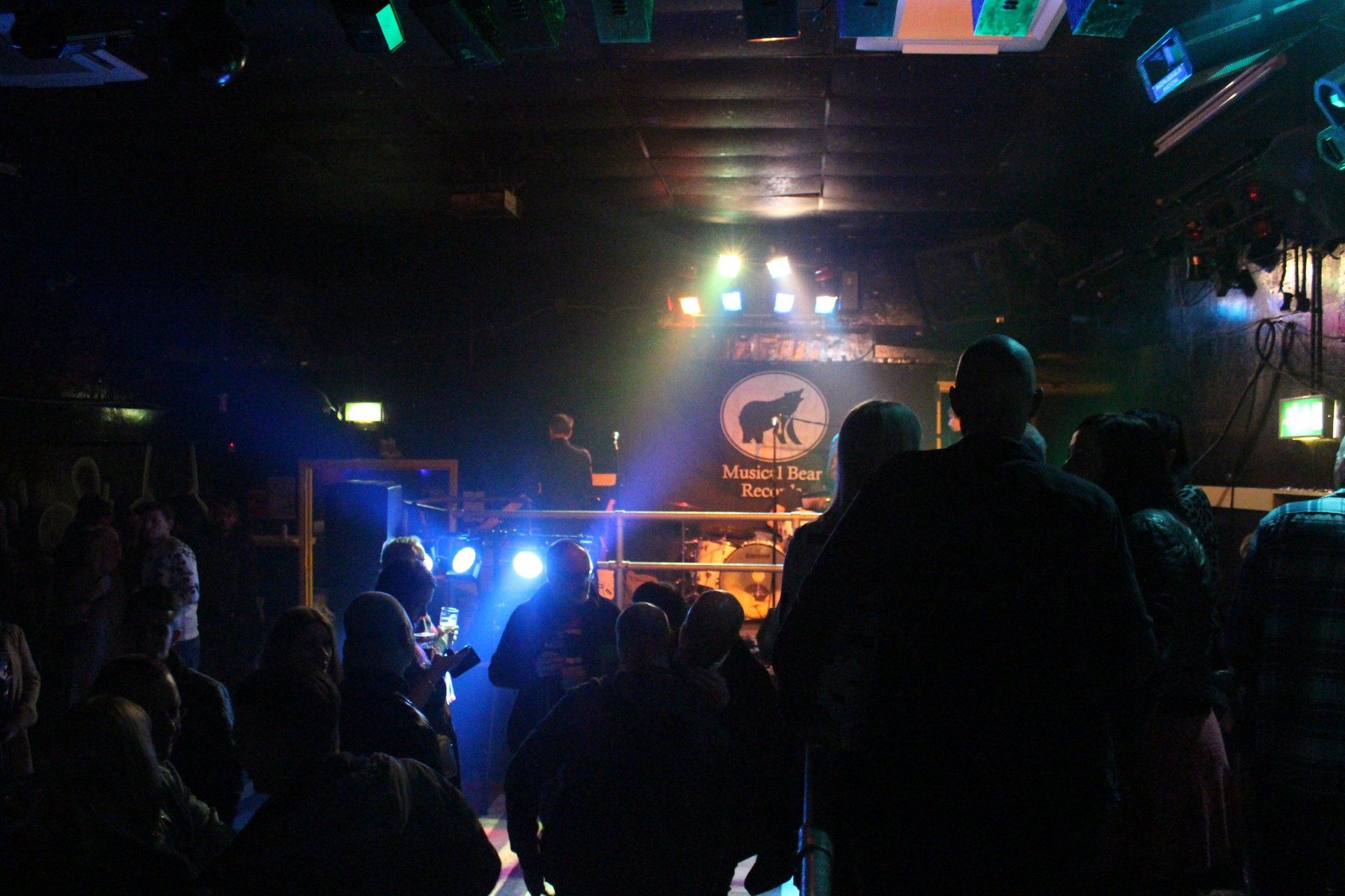 A crowd of people are standing in front of a stage in a dark room.