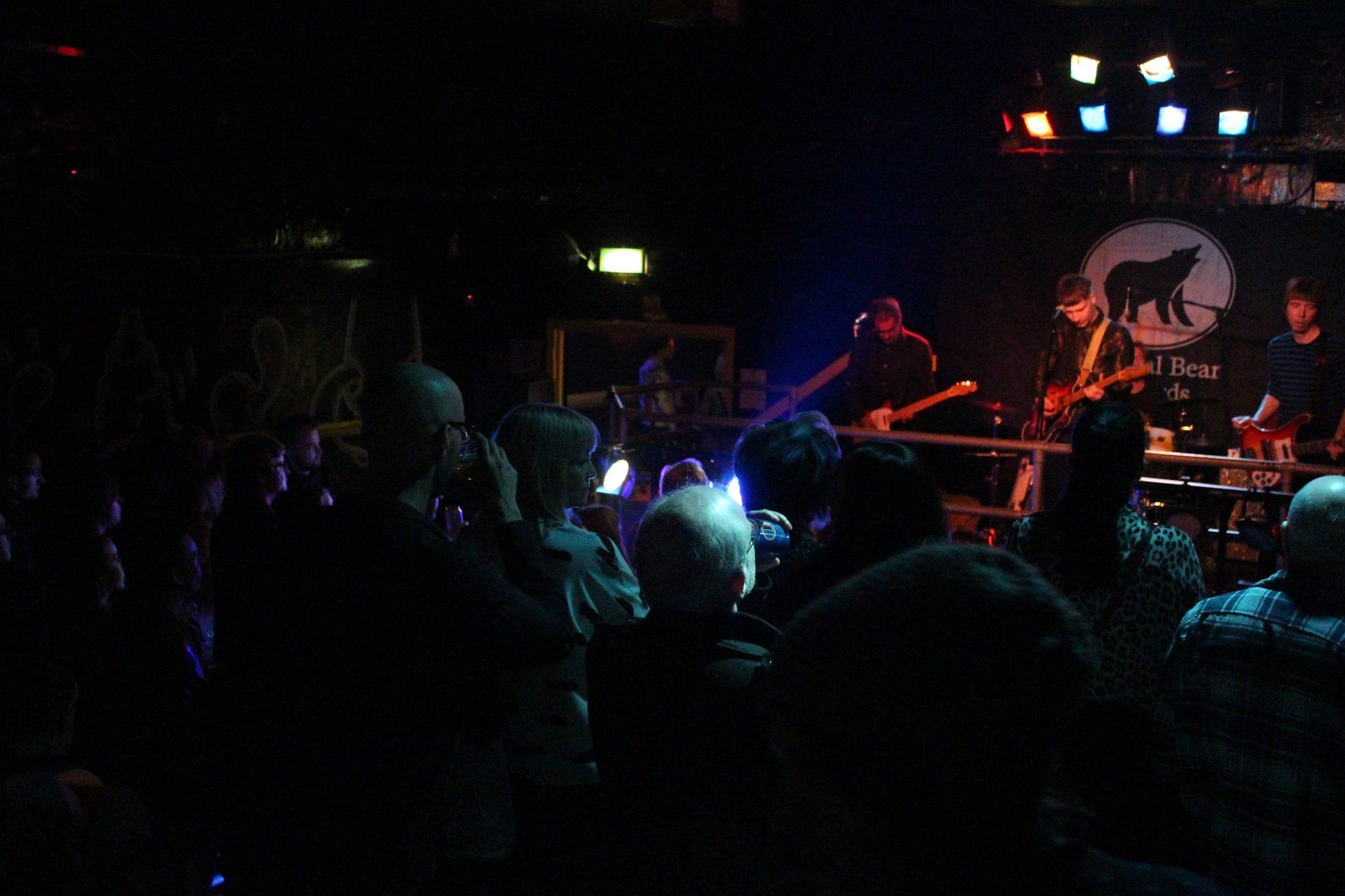 A crowd of people are watching a band on stage in a dark room.