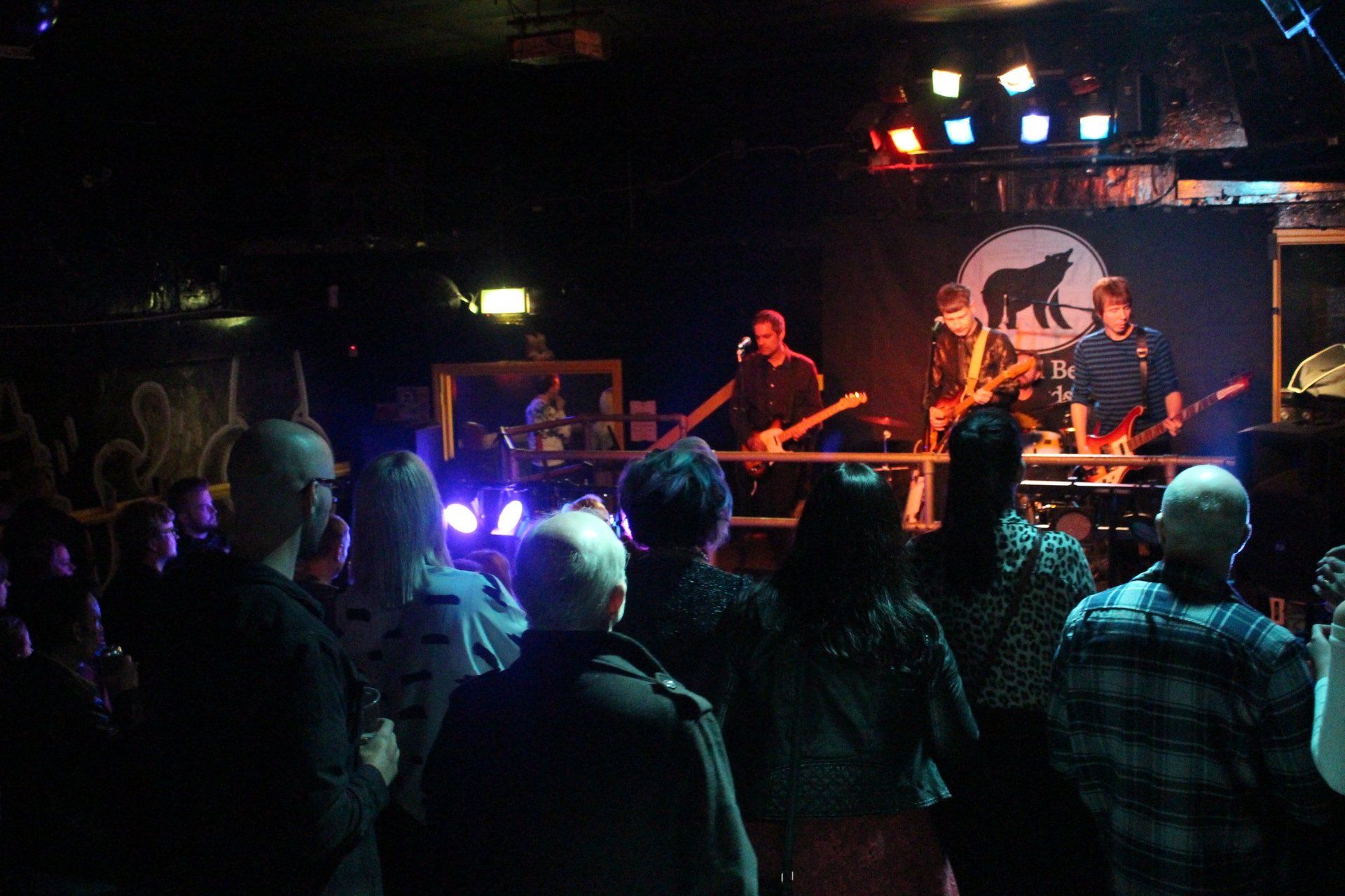 A crowd of people are watching a band on stage in a dark room.