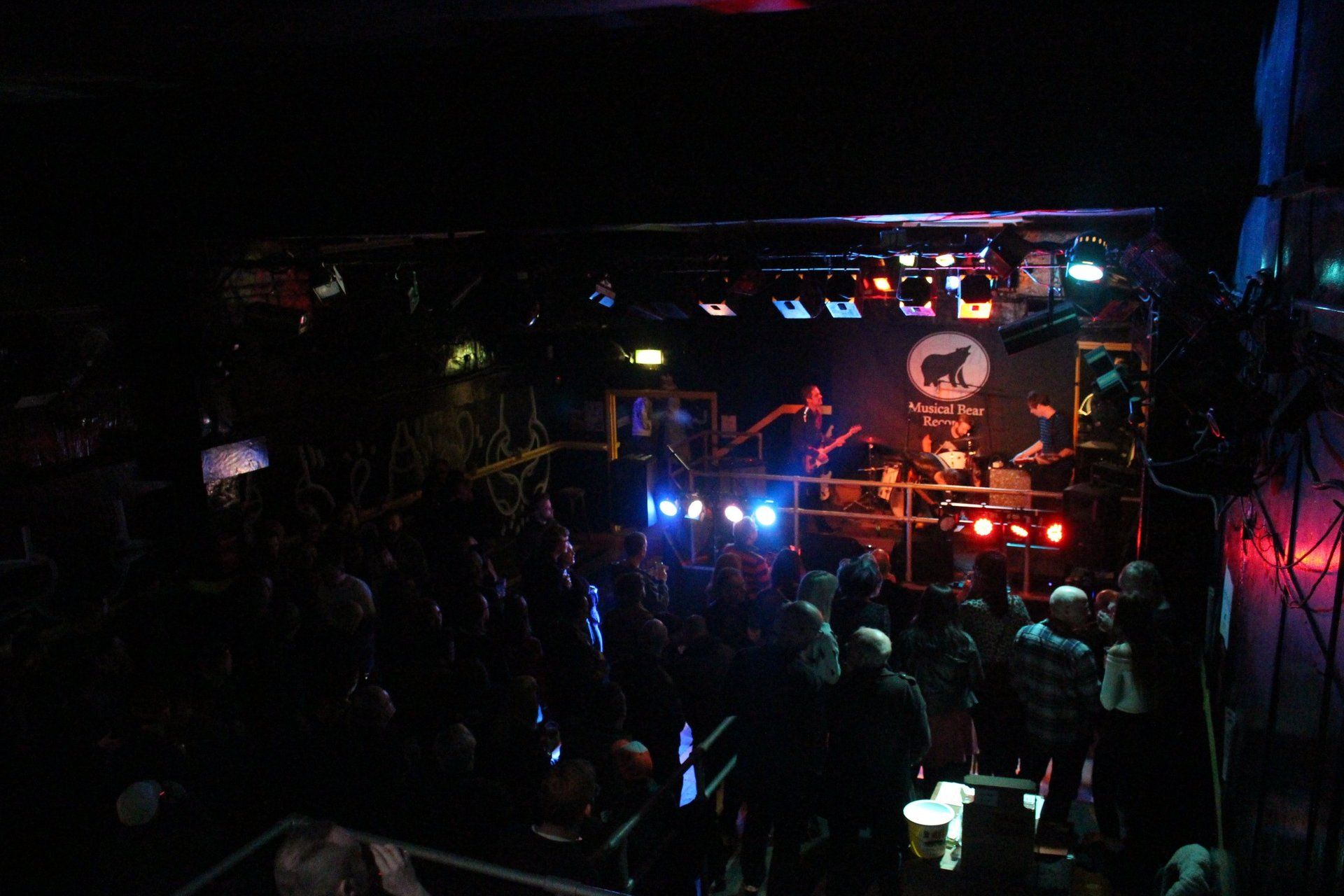 A crowd of people are sitting in a dark room at a concert.