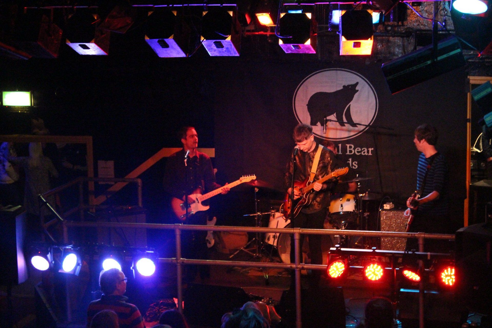 A group of people playing instruments on a stage in front of a sign that says bear