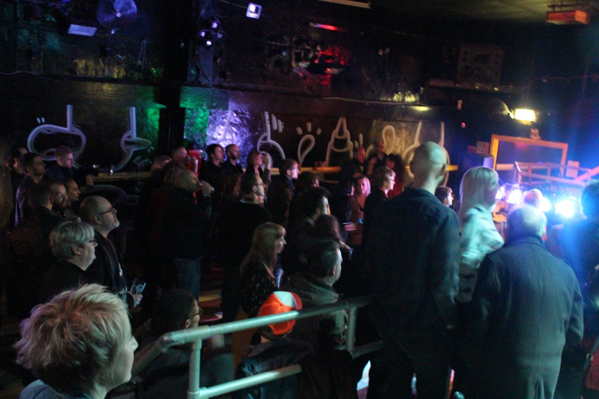 A crowd of people are gathered in a dark room with a sign on the wall that says 