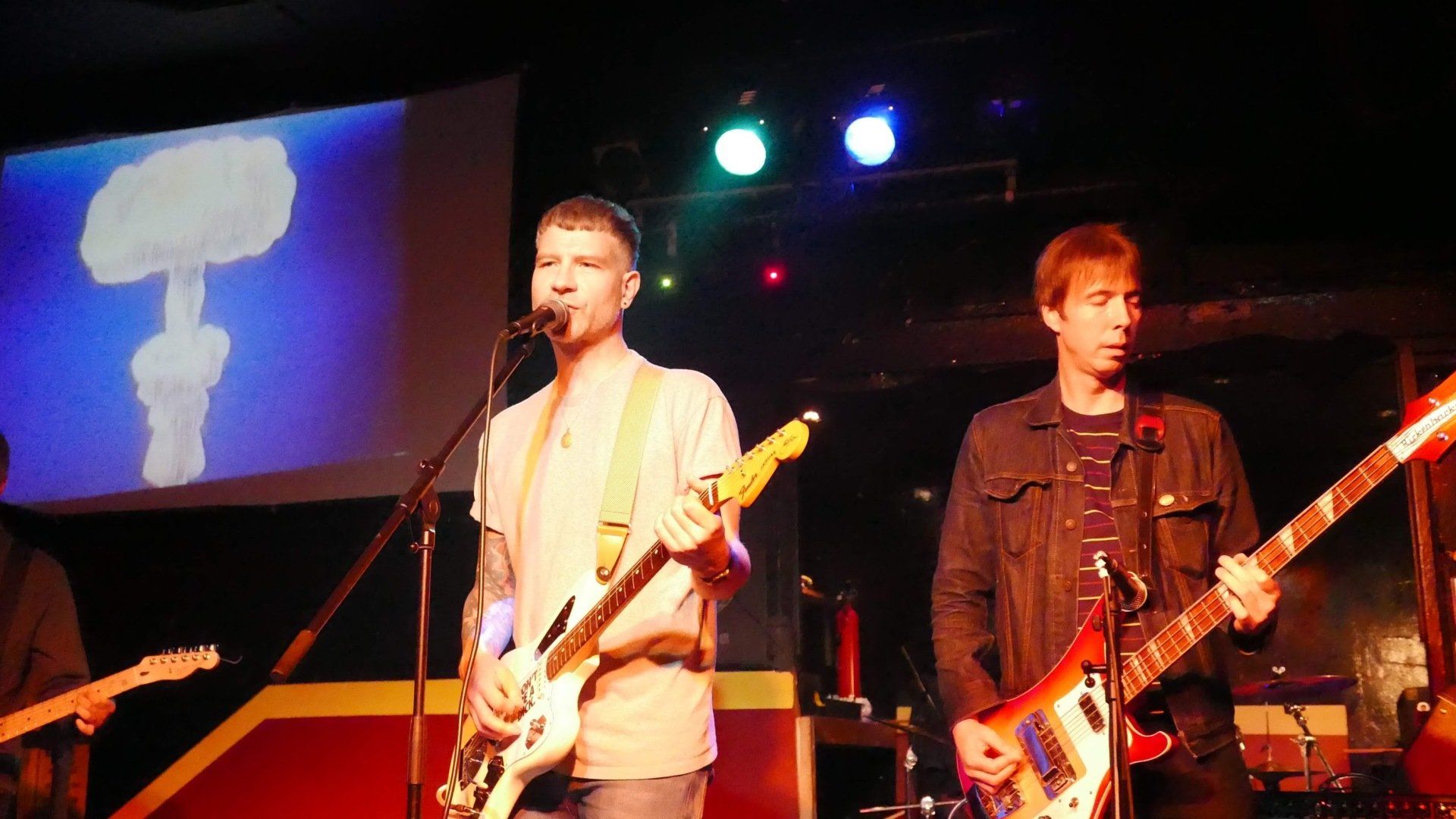 A man singing into a microphone while another man plays a guitar