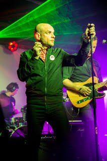 A man is singing into a microphone on a stage while another man plays a guitar.