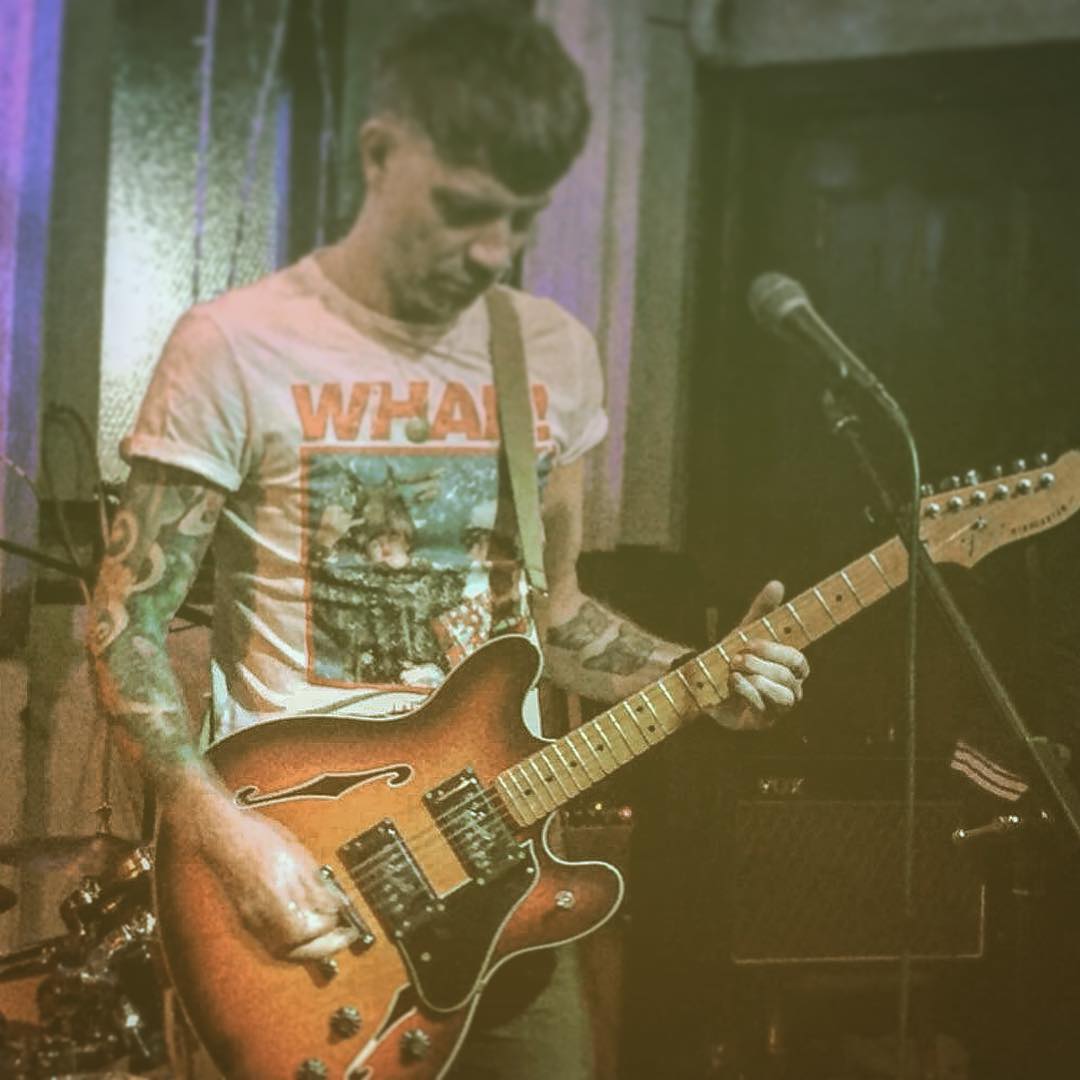 A man wearing a shirt that says what is playing a guitar
