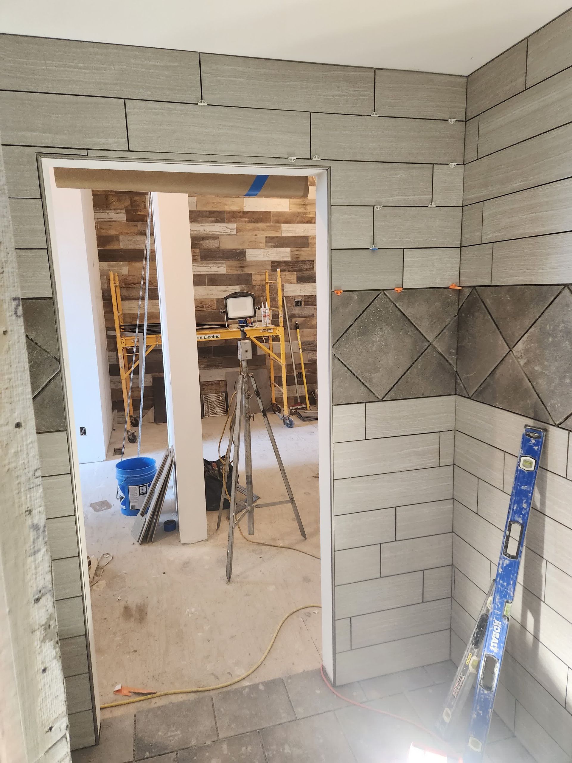 A person is laying tiles on a wall with a trowel.