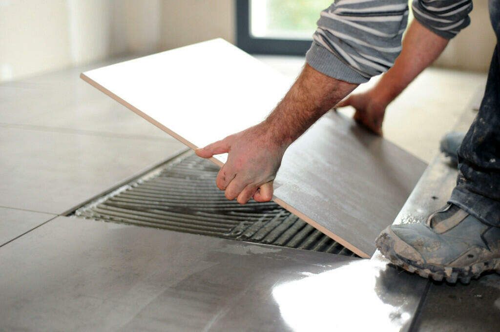 A person is laying tiles on a wall with a trowel.