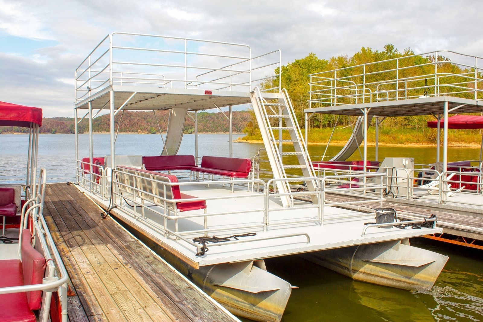 Pontoon boats docked on a lake, featuring two levels, red seating, and a white metal frame.