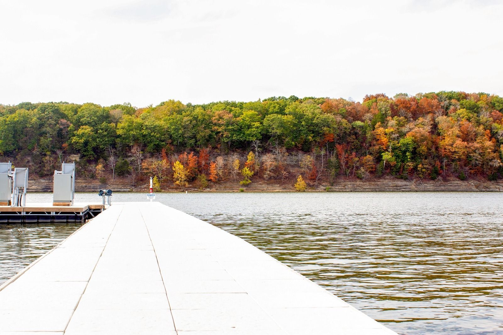 White dock extends into lake, with colorful autumn trees on the far shore.