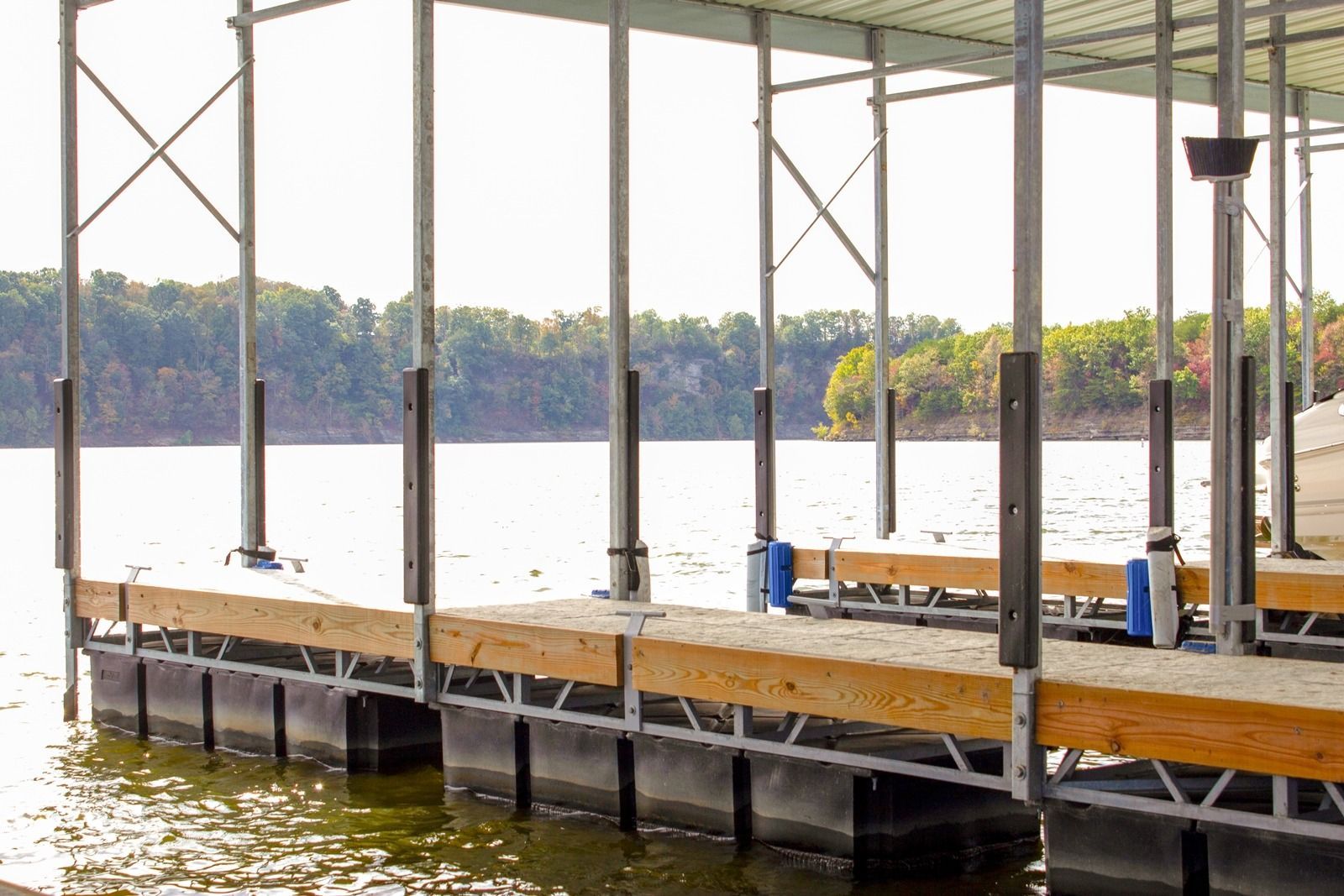 Dock with a covered walkway on a lake. Black floats, metal supports, and wood decking.