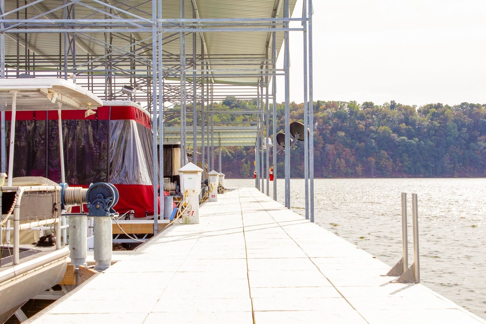 Dock with boats under a metal roof. Water and trees in the background.
