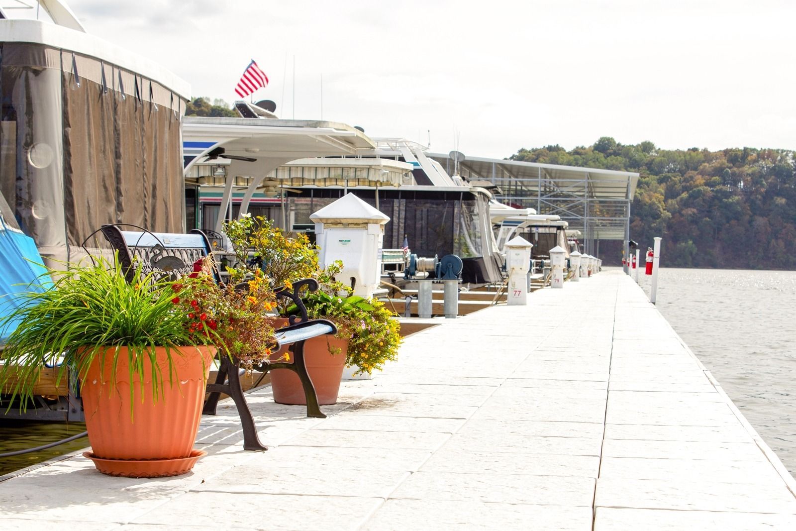 A row of boats docked at a pier with potted plants and a US flag, overcast sky.