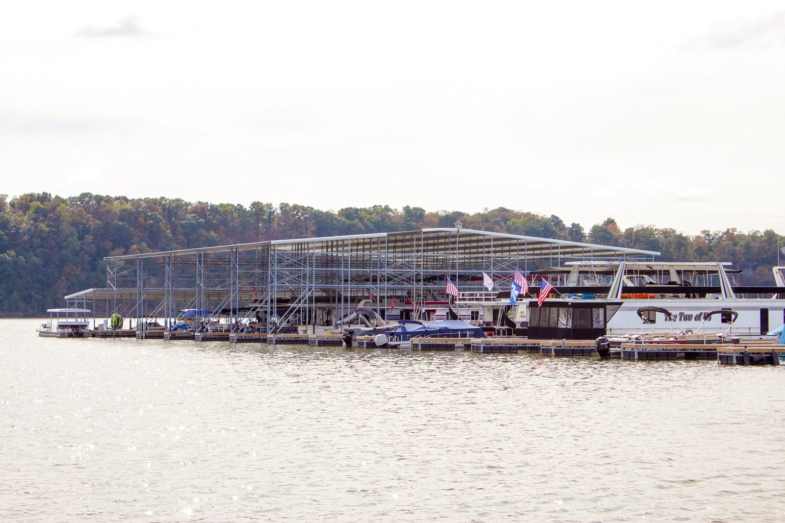 Boats docked at a marina on a lake, with metal structures and trees in the background.