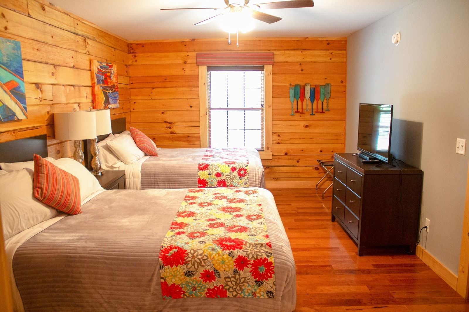 A bedroom with two beds, wood panel walls, and a TV.