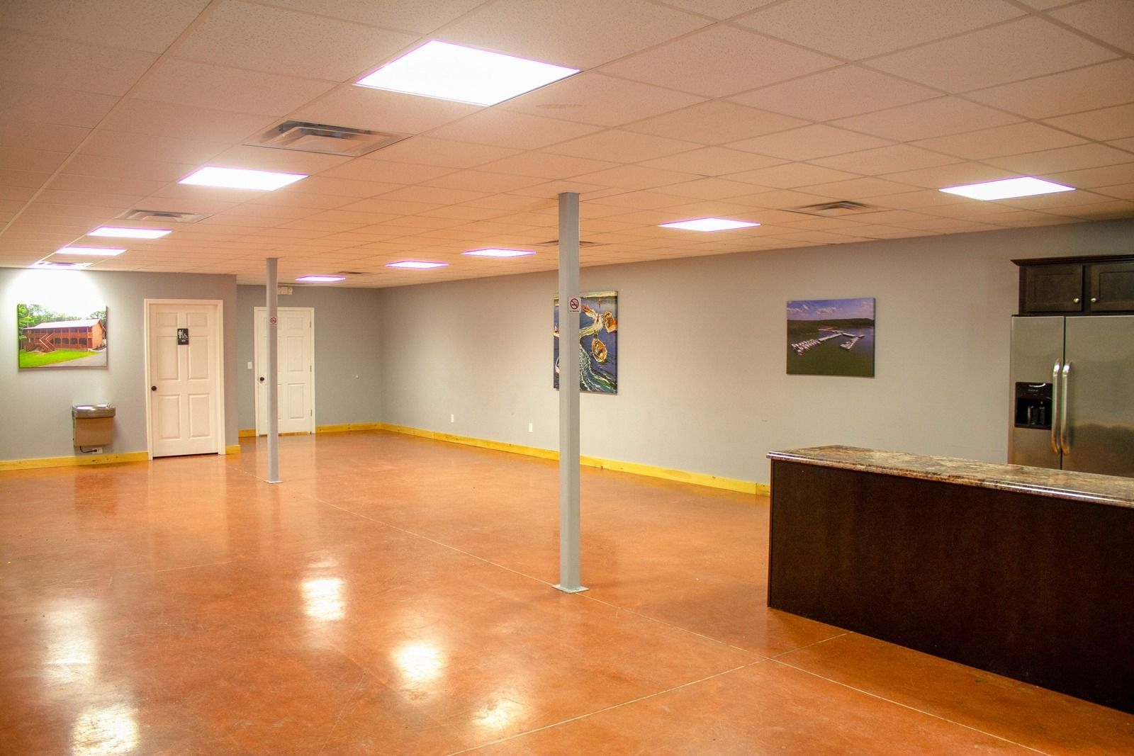 Large, open room with brown floor, gray walls, recessed lights, and stainless steel appliances.
