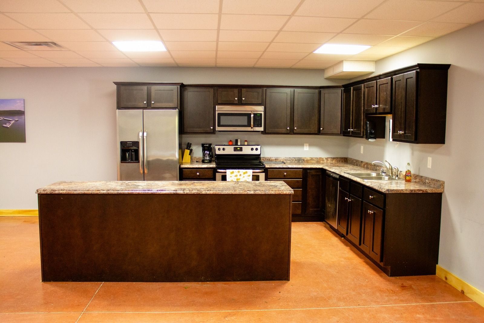 A large, dark-brown kitchen with stainless steel appliances, granite countertops, and an island on a brown floor.