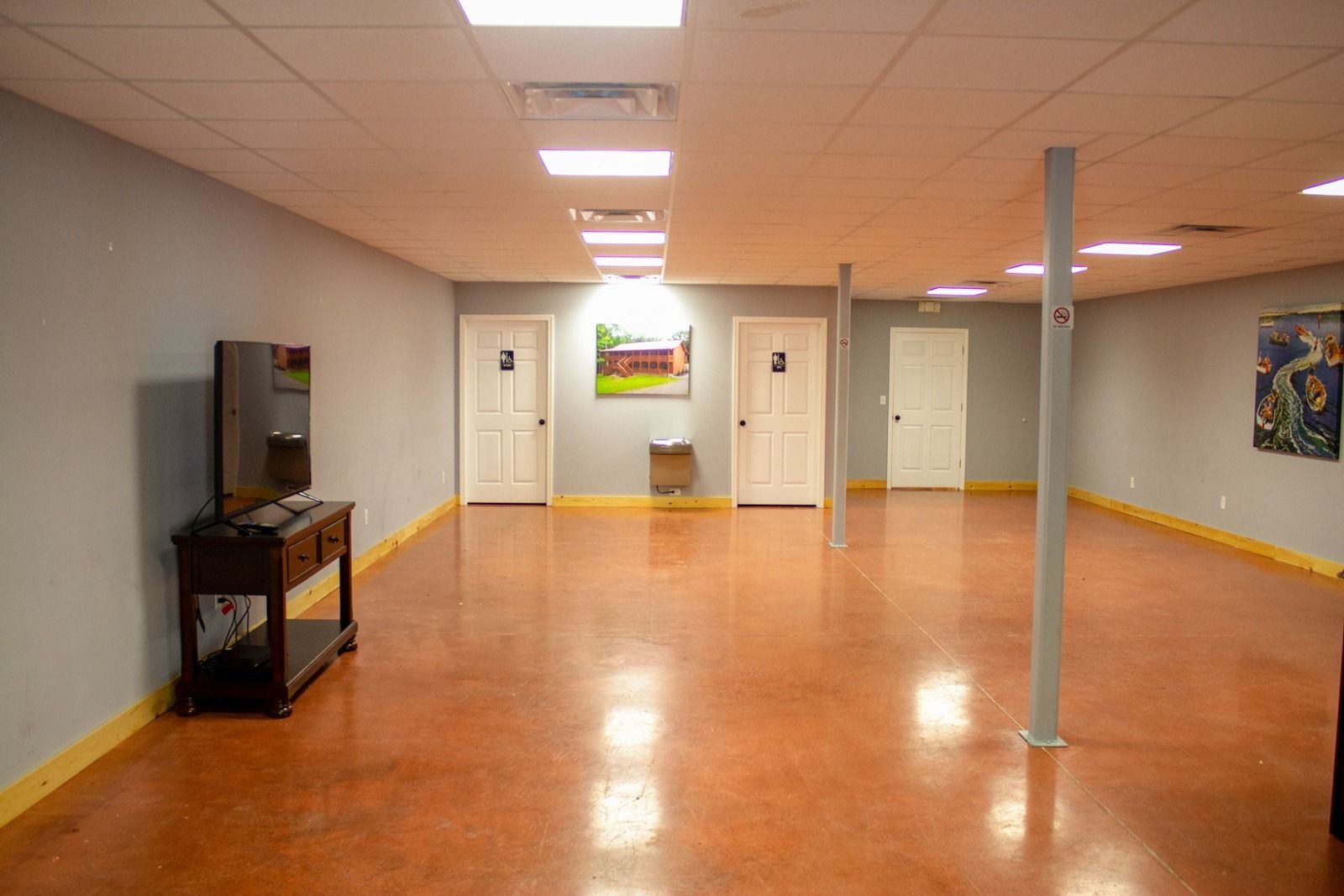 Spacious room with polished red-brown floor, pale blue walls, doors, TV, and support columns.