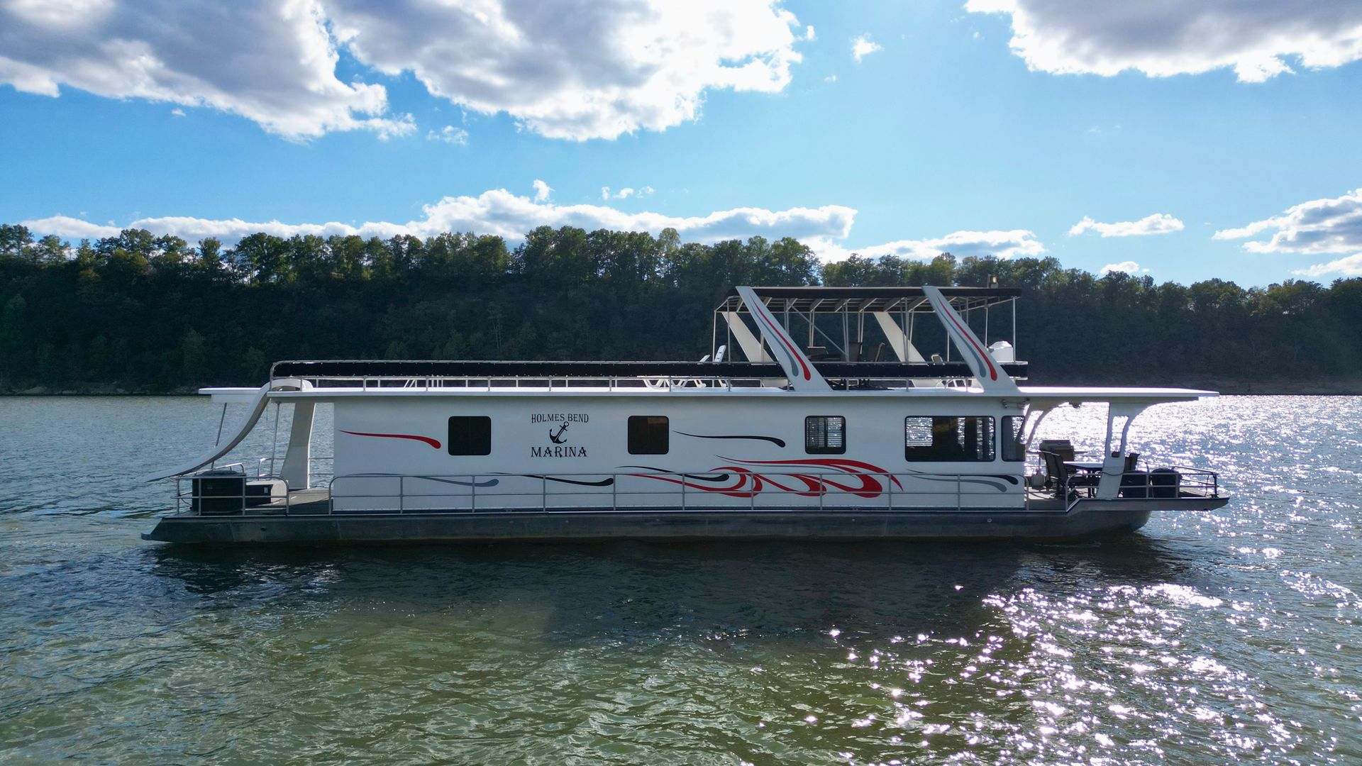 Houseboat on a lake, black roof and windows, white and red trim, trees in background.