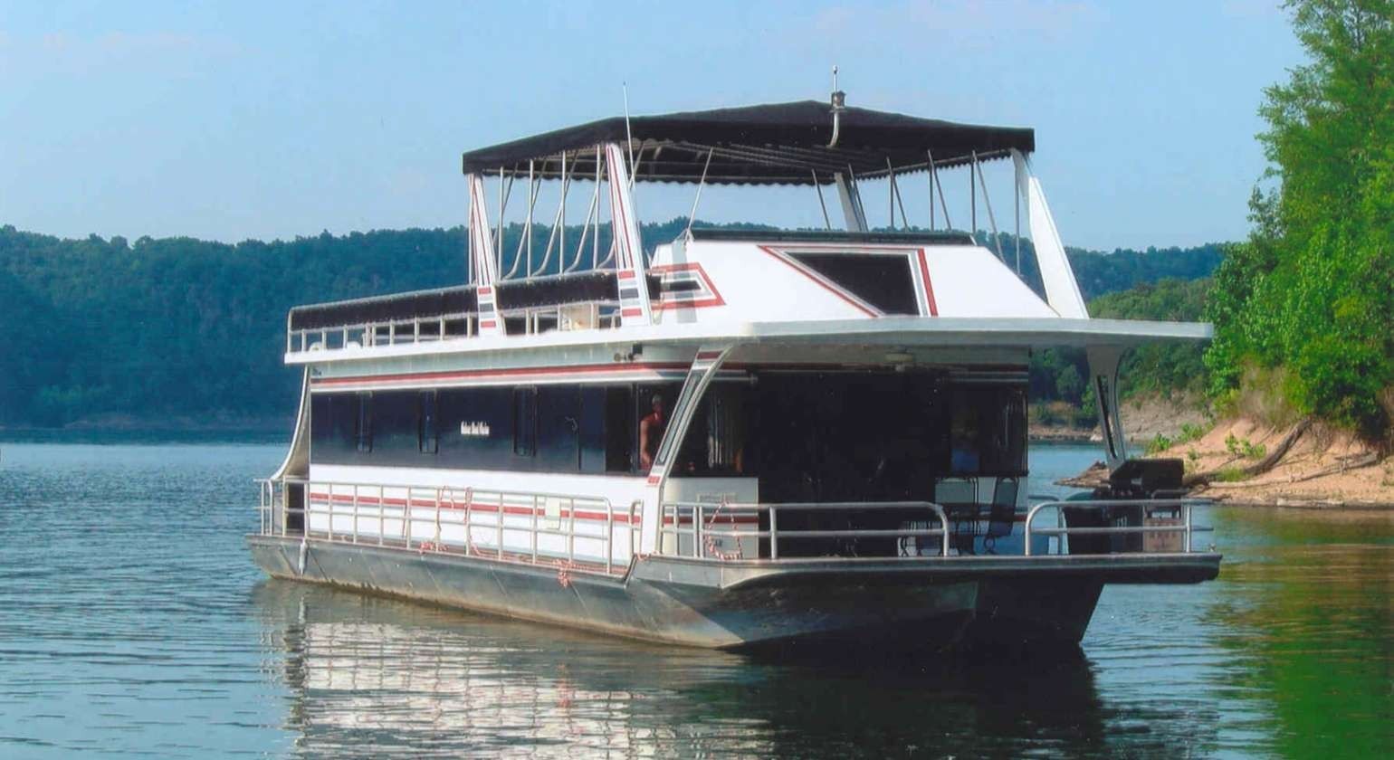 Houseboat on a lake, black roof and windows, white and red trim, trees in background.