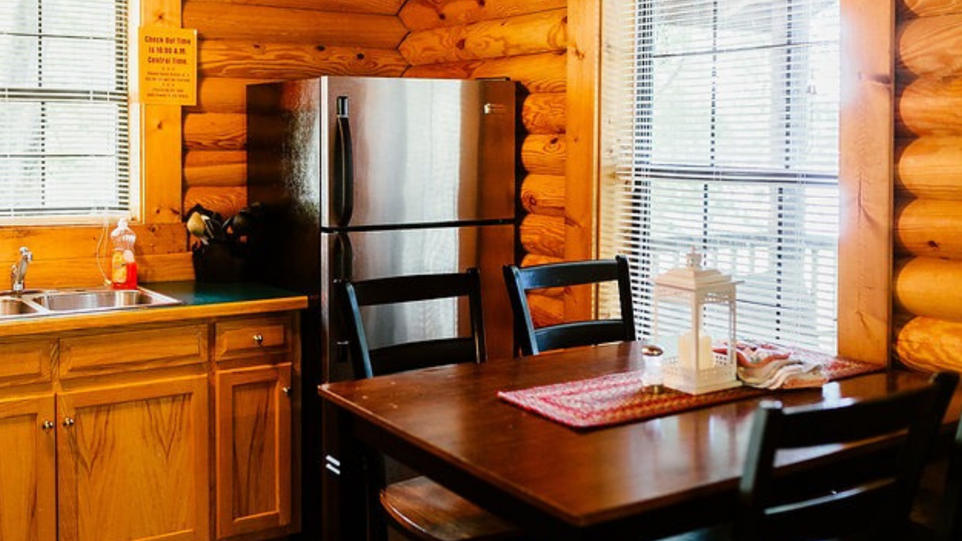 Log cabin kitchen with stainless steel refrigerator, wooden table, and cabinets.