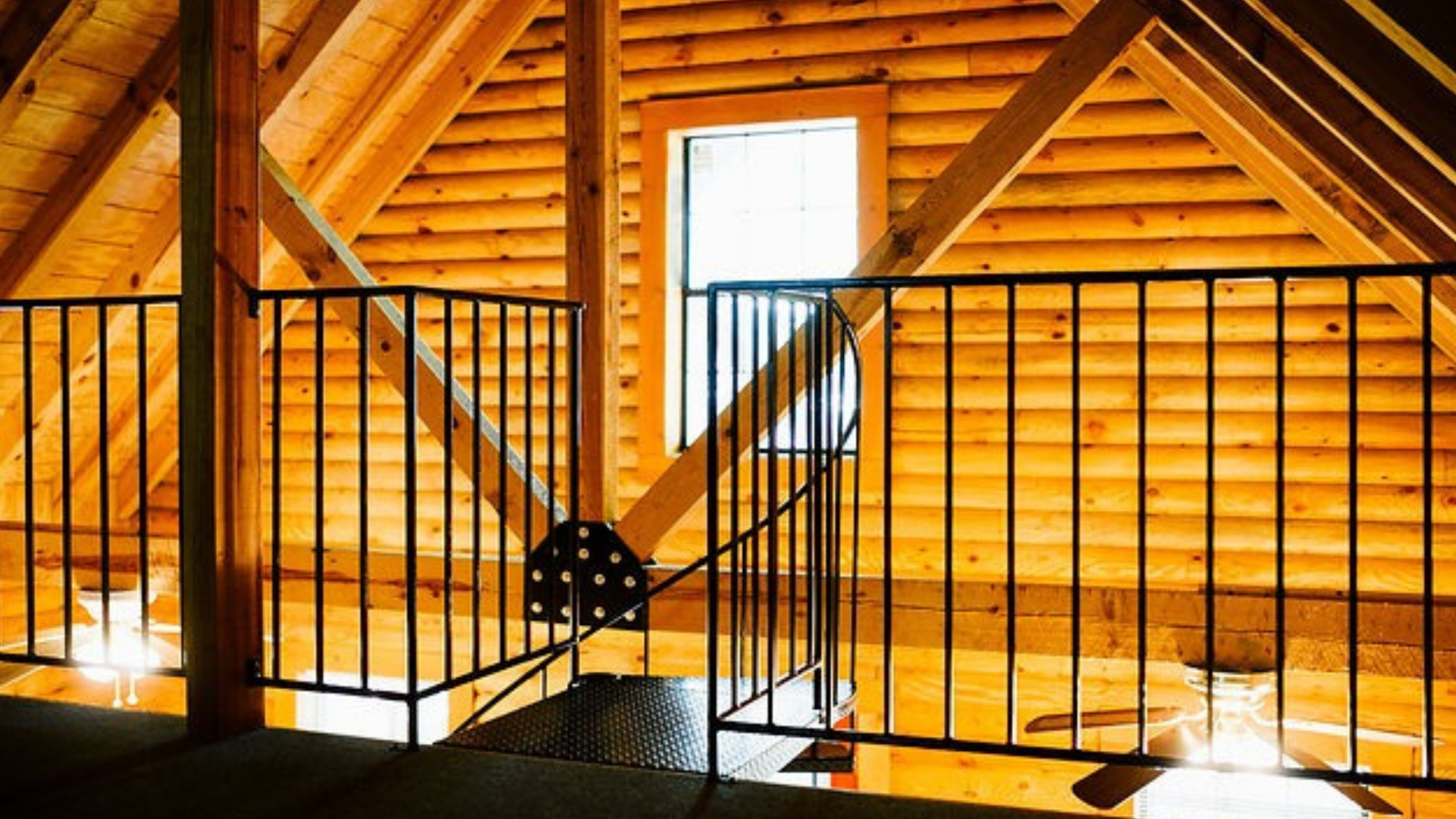 Interior loft with black railing, wood beams, and window.