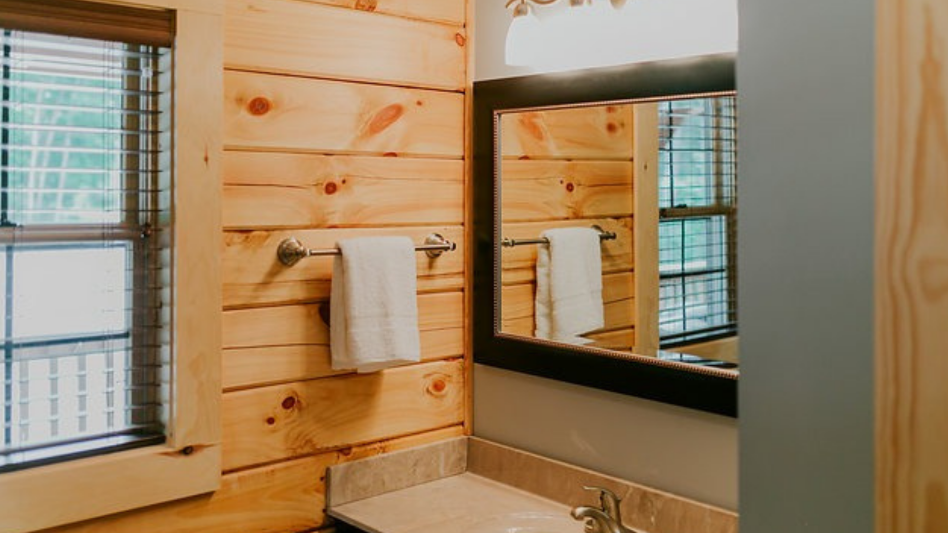 Bathroom with wood paneling, a mirror, towel rack, and window with blinds.