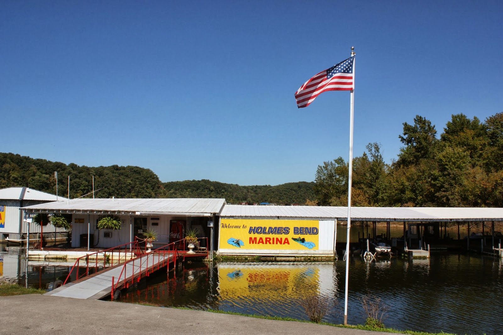 Marina on a lake with a building, dock, boats, and American flag under a blue sky.