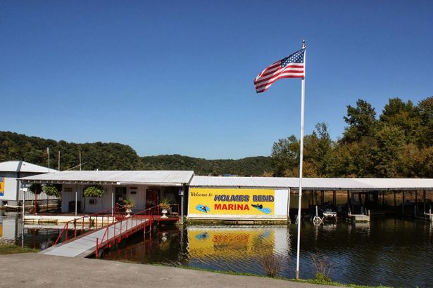 Marina on a lake with a building, dock, boats, and American flag under a blue sky.