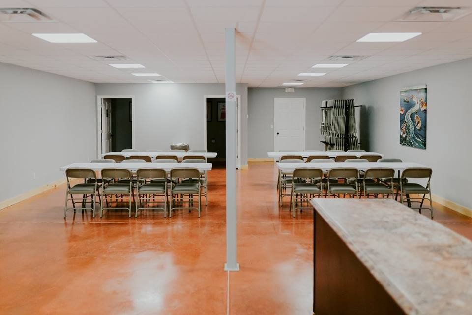 An event space with tables, chairs, and a bar. The floor is reddish-brown, and walls are light blue.