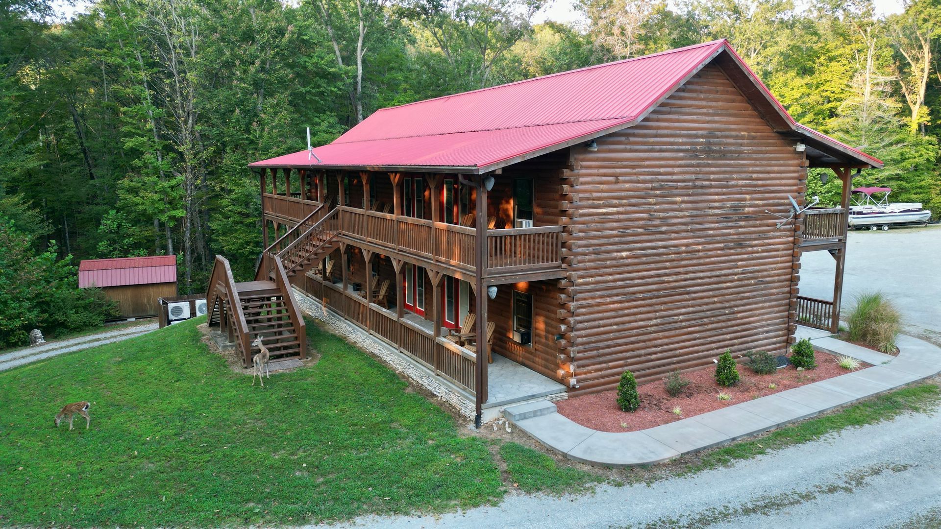Log cabin with red roof, two-story, outdoor staircases, and surrounding trees.