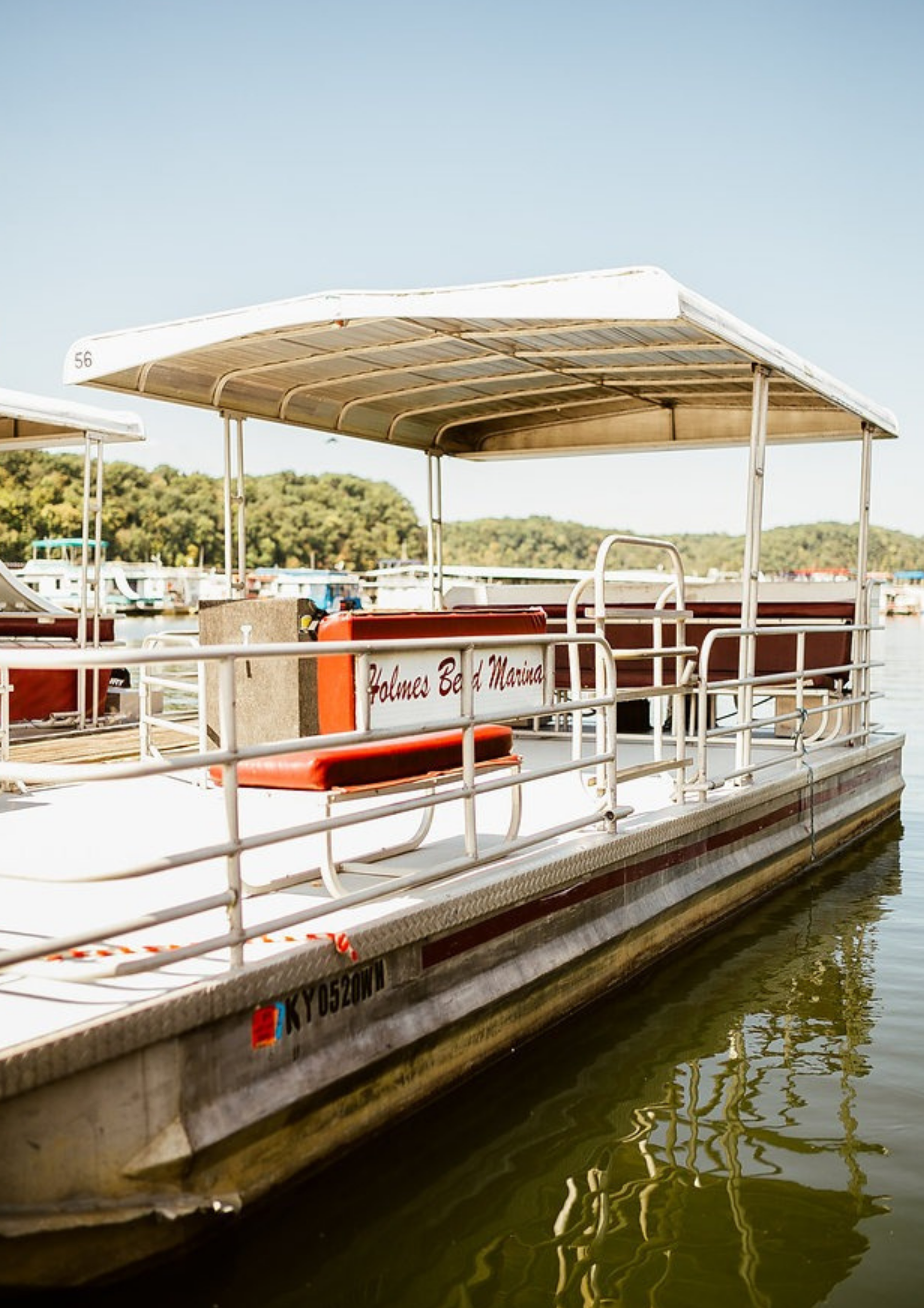 Pontoon boat at a dock on the water with red seating and a white awning; sunny day.