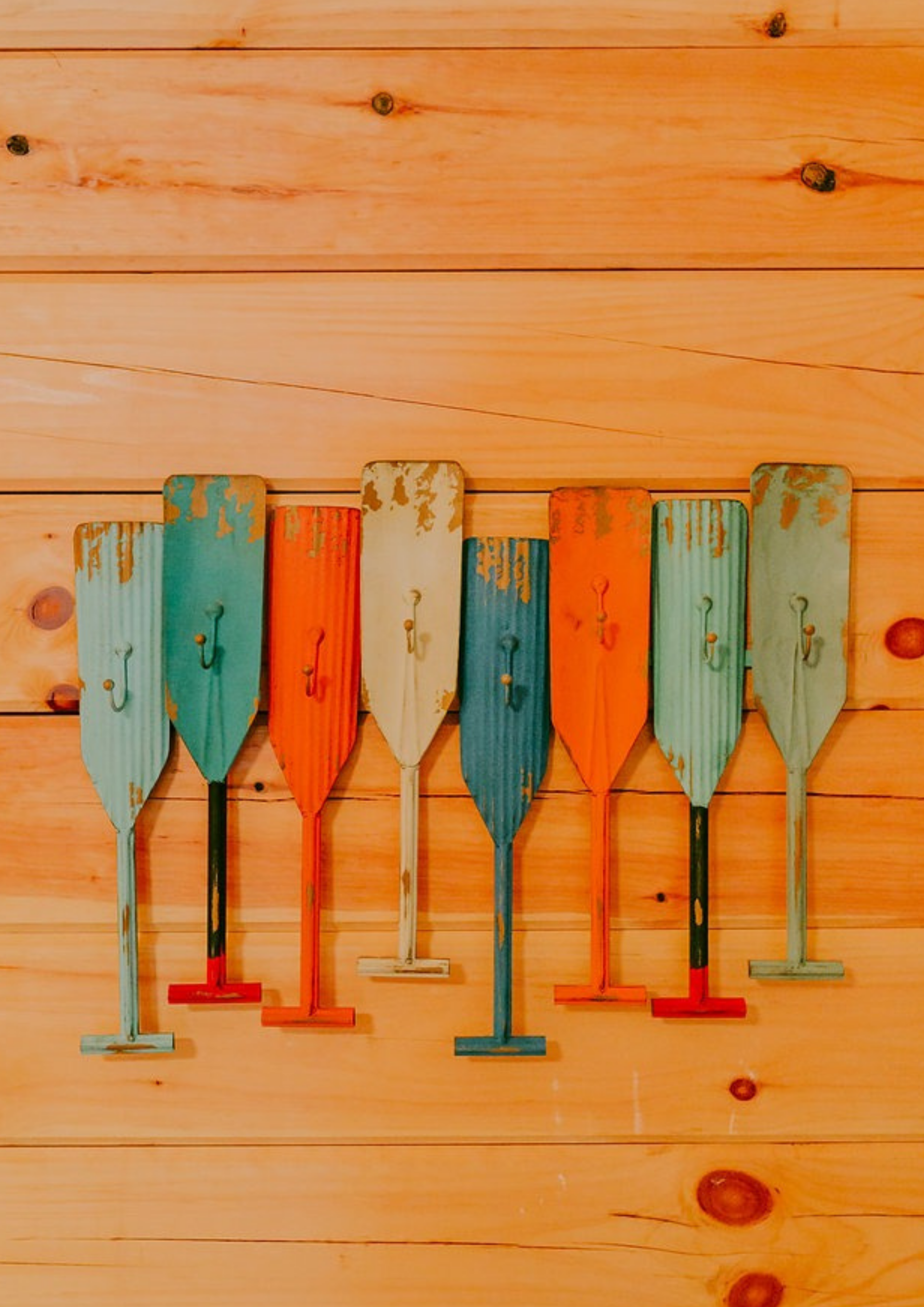 Row of colorful, weathered oars mounted on a light wood wall.