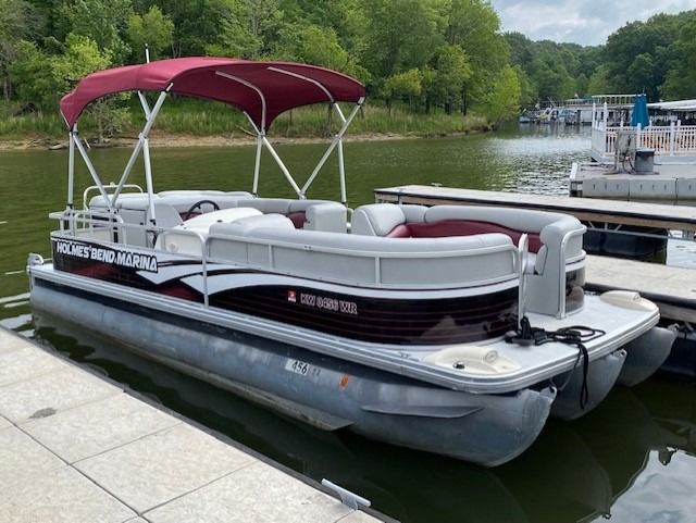Pontoon boat docked at a pier with burgundy canopy and accents on the side.