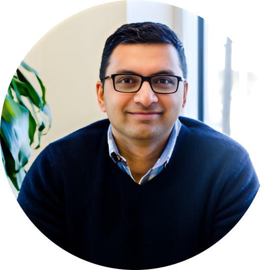 A man wearing glasses and a black sweater looks at the camera