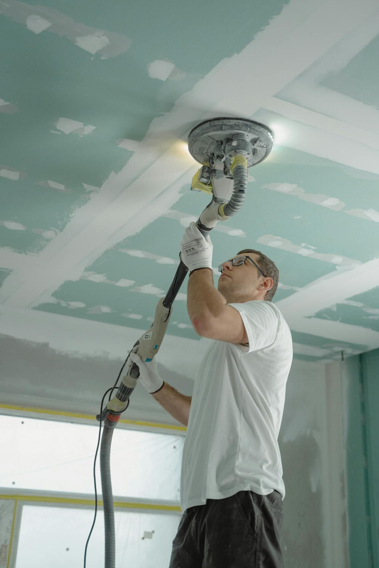 A man is sanding a ceiling with a sander.