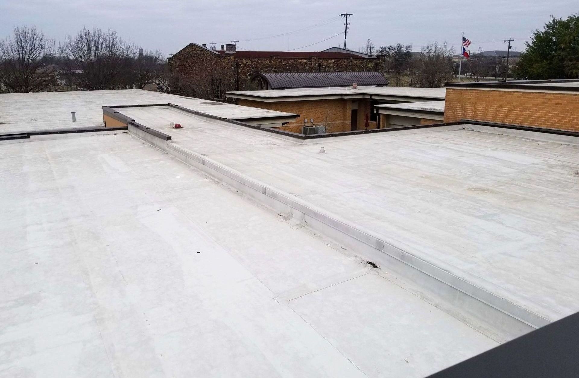 The roof of a building with a white roof and trees in the background.