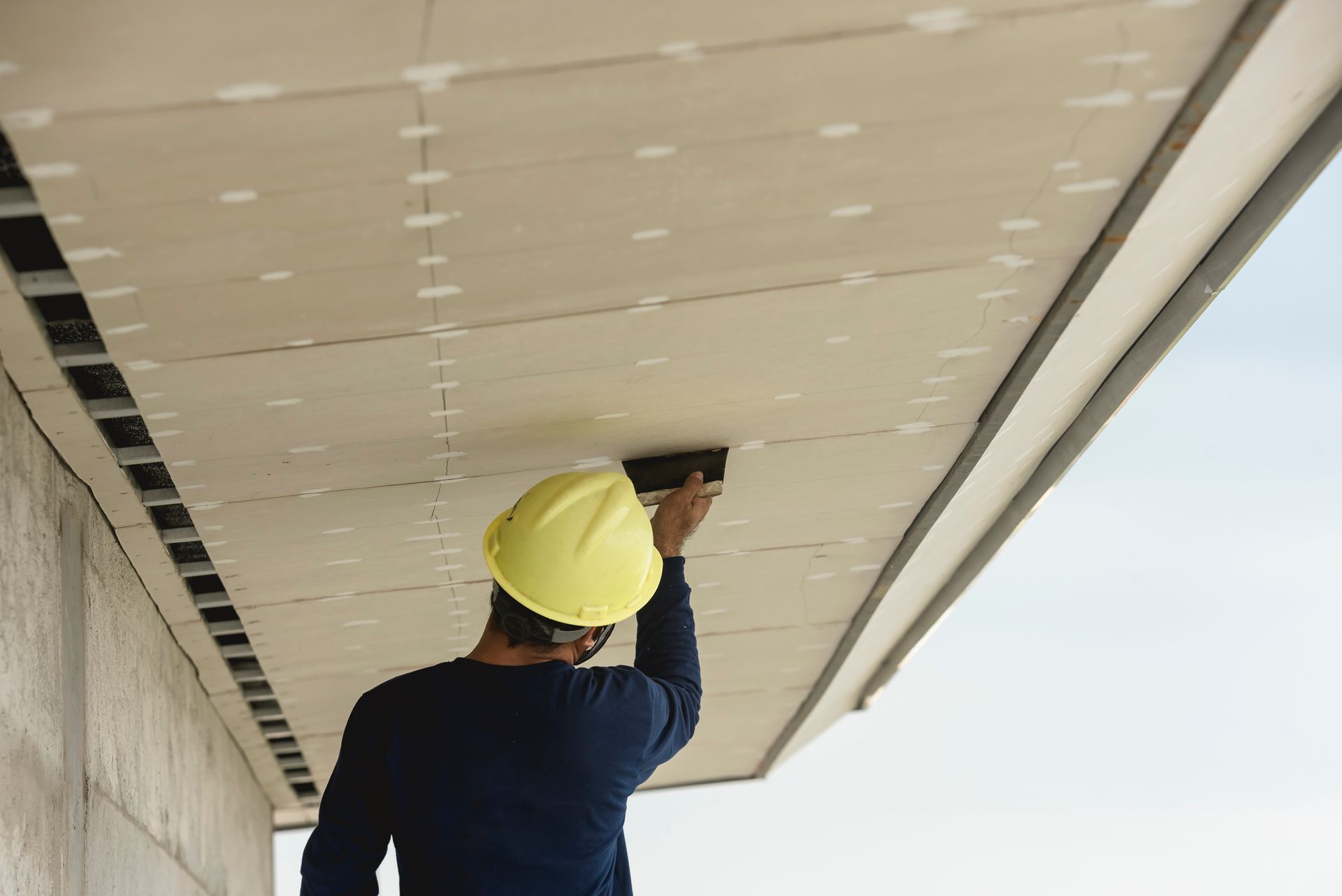 A man wearing a hard hat is working on the ceiling of a building.