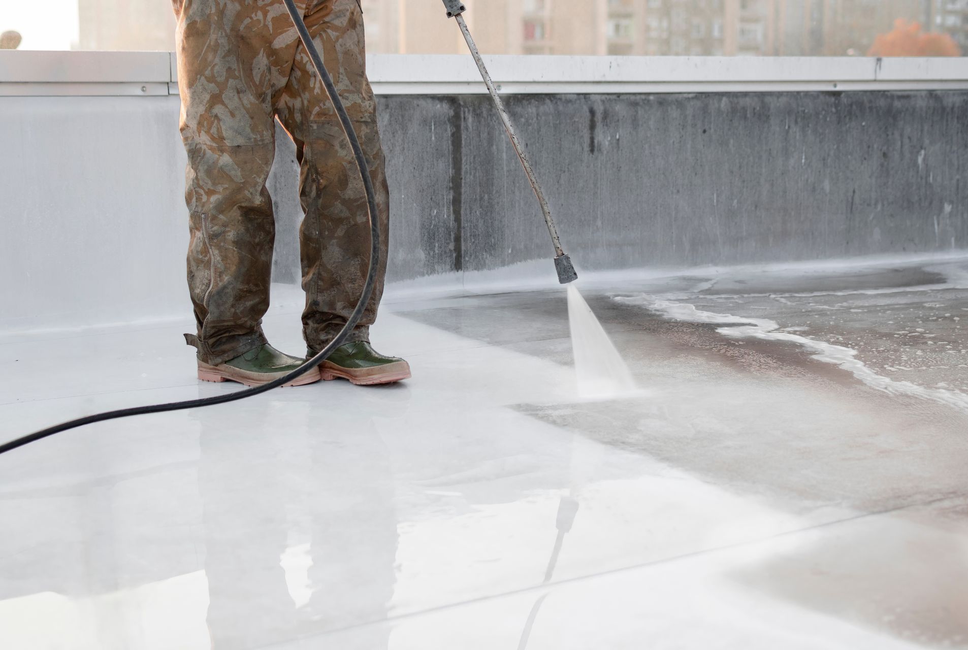 A man is using a high pressure washer to clean a roof.