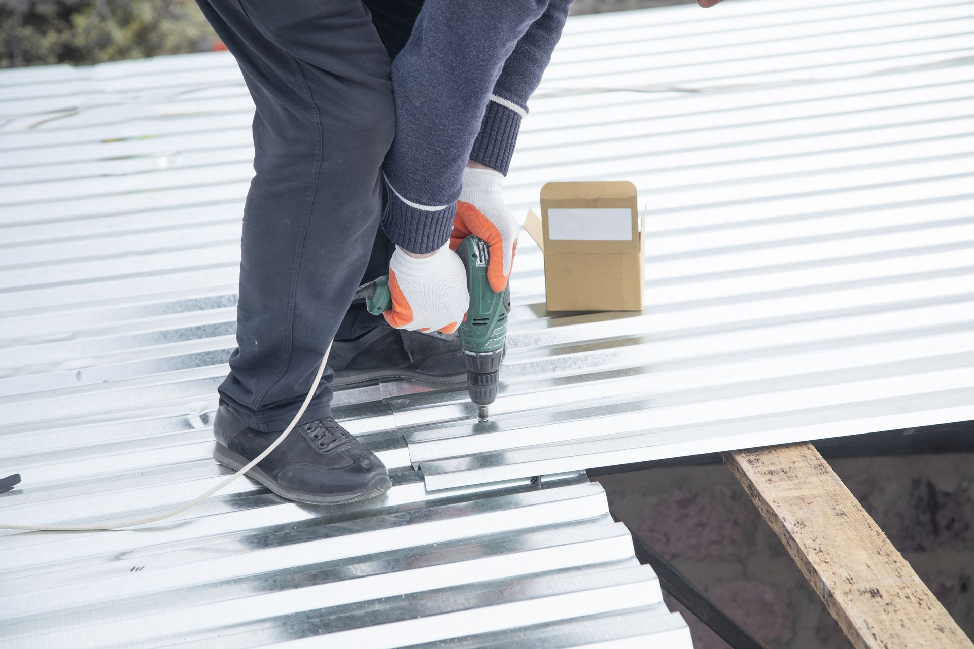 A man is using a drill on a metal roof.