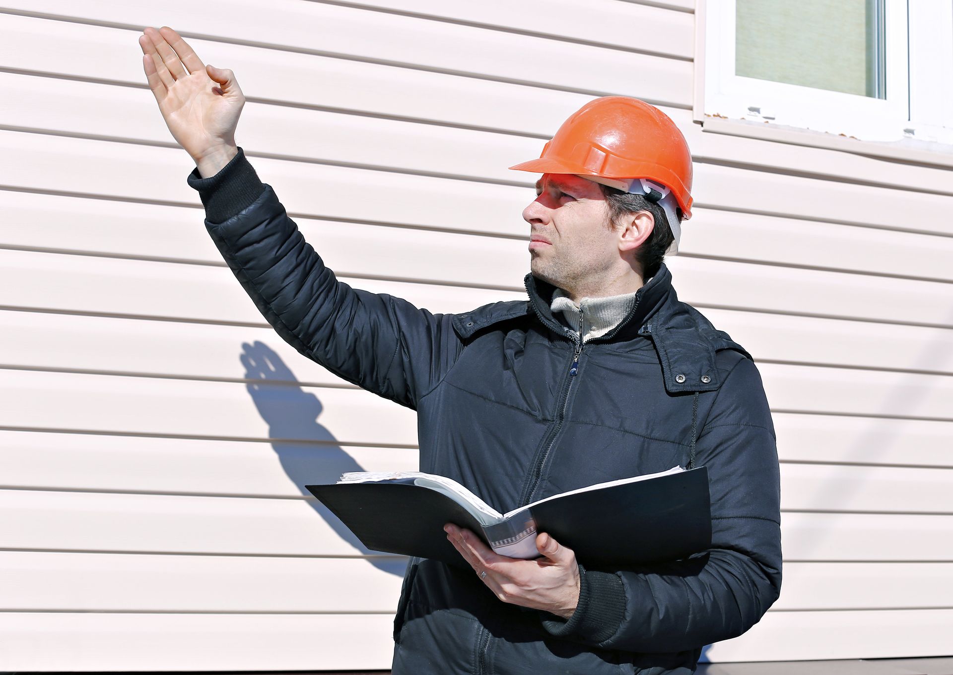 The man is wearing a hard hat and holding a clipboard.